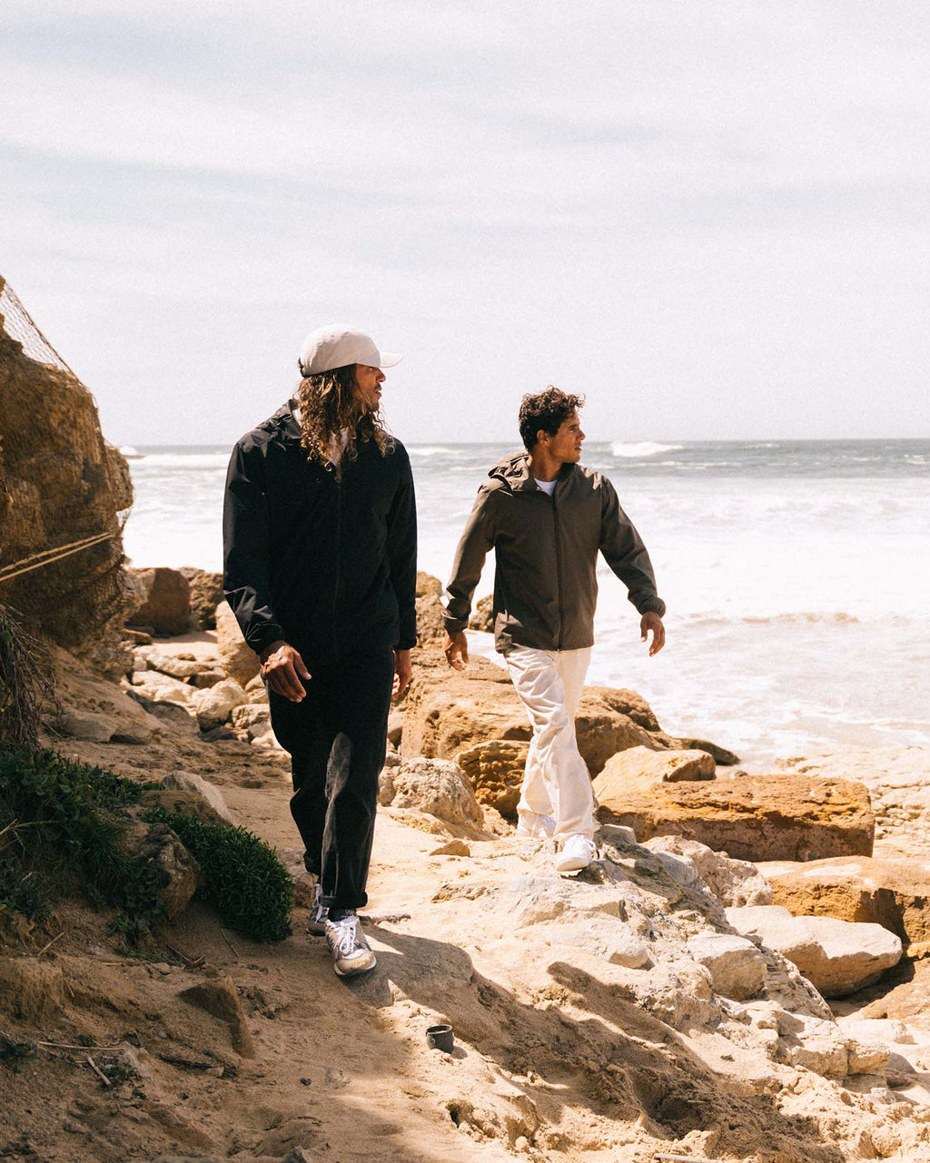 Two people walking along a rocky path by the ocean.