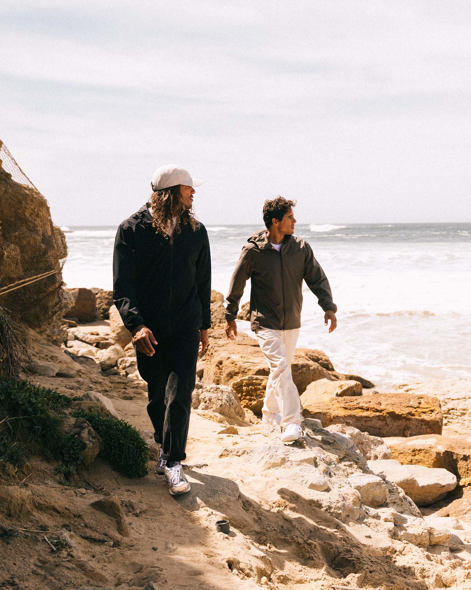 Two people walking along a rocky path by the ocean.