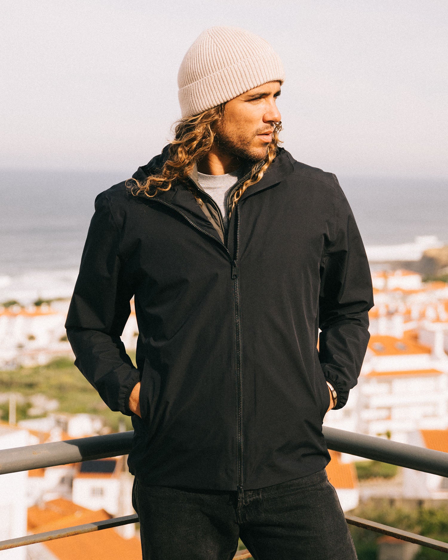 Person wearing a black jacket and beige beanie standing outdoors with a scenic background