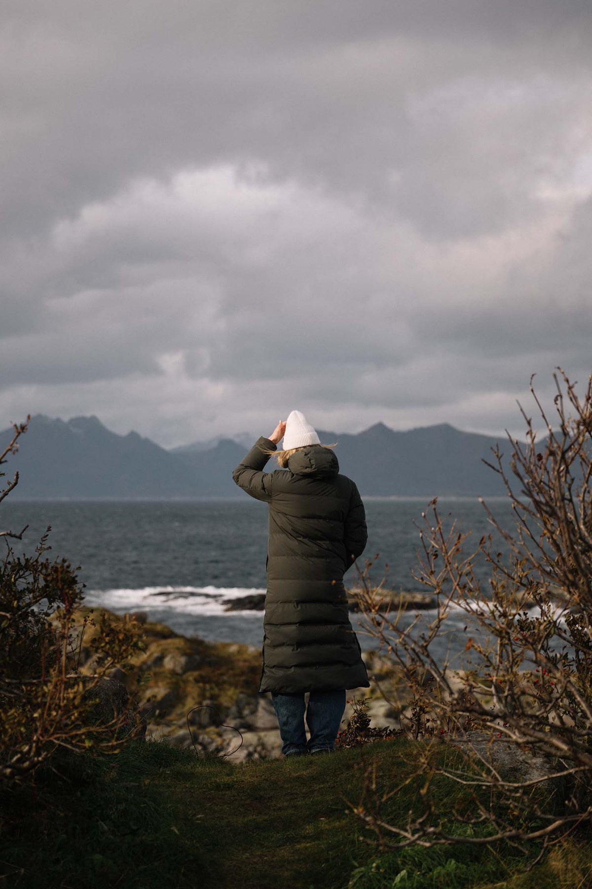 Person standing on a cliff overlooking the ocean with mountains in the background