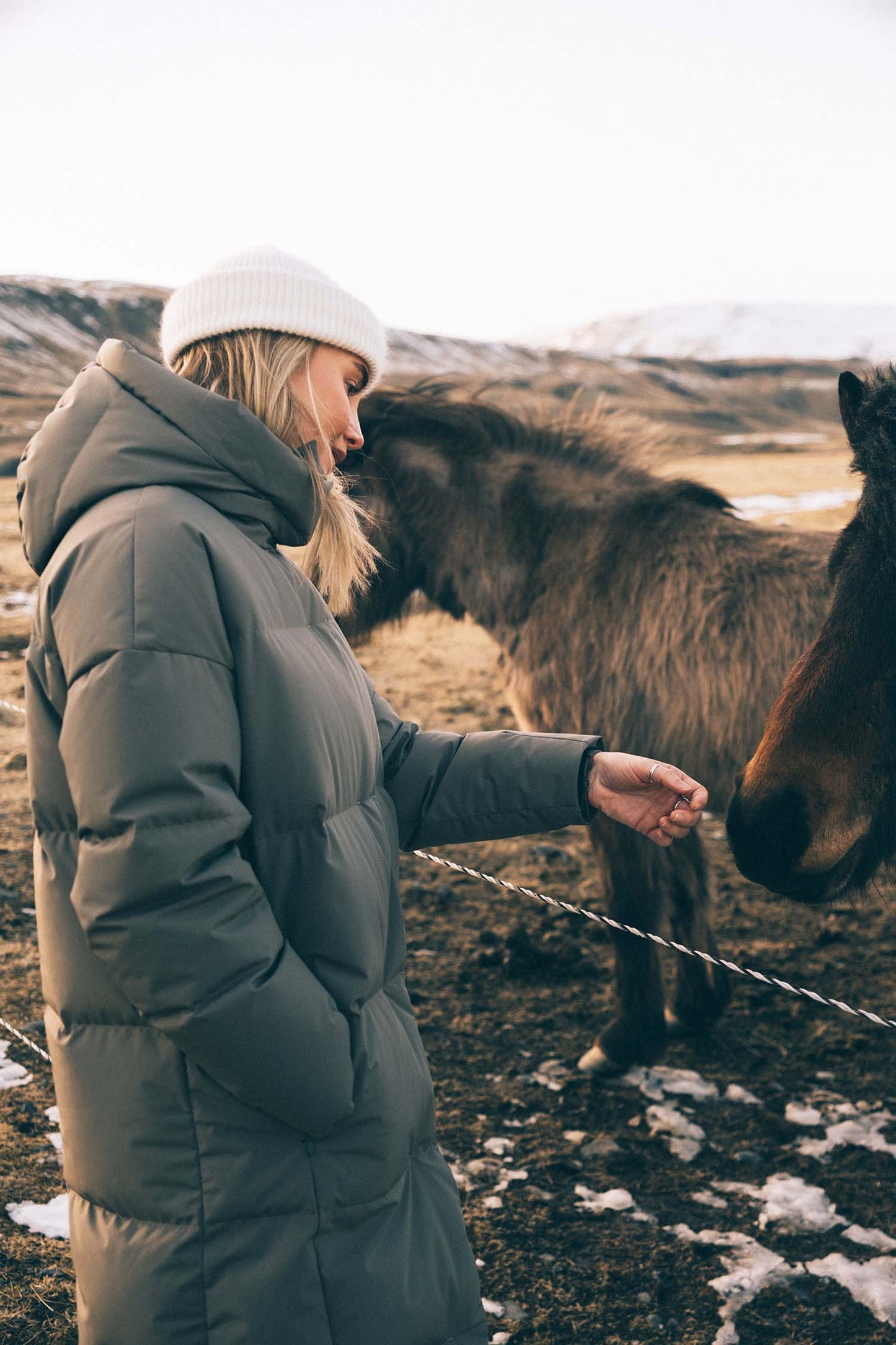 Person in a puffer jacket interacting with a horse in a field