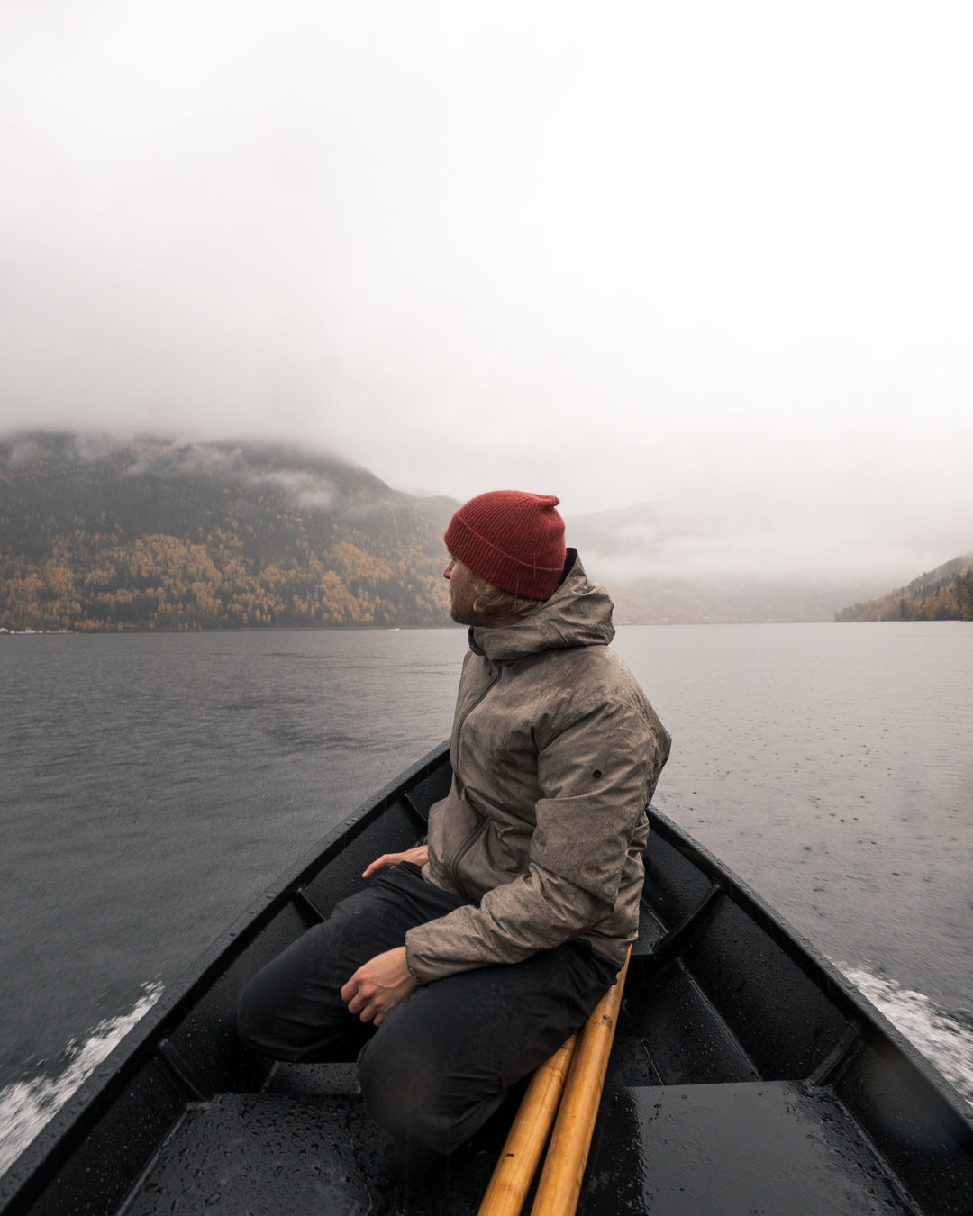 Man in a red beanie sitting in the bow of the boat, looking out over the lake