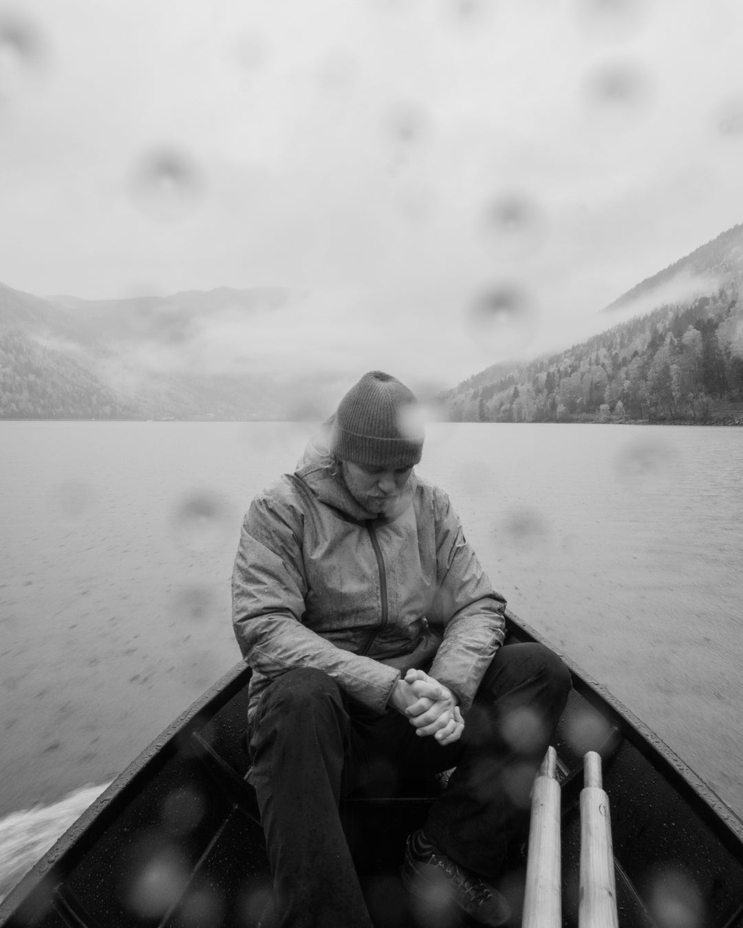 Black and white photo of a man sitting in the bow of the boat with rain on the lens