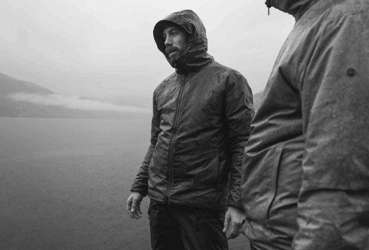 Black and white photo of a man in a hooded jacket in heavy rain by the lake